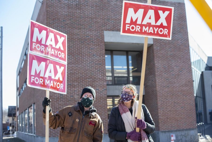  UVM Senior Ethan Waxman and UVM Alumni Mariah Cronin stand outside the Fletcher Free Library, the Ward 8 polling location, holding up signs for Max Tracy March 2.