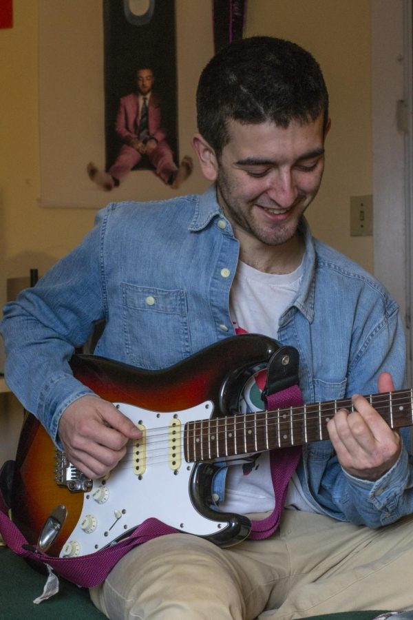 Luban sits playing his guitar in front of a Mac Miller poster April 2.