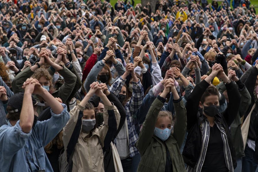 Student protesters clasp their hands together and raise them over their heads, mimicking the motion displayed by Hendrick as they stand on top of the Waterman steps May 3.