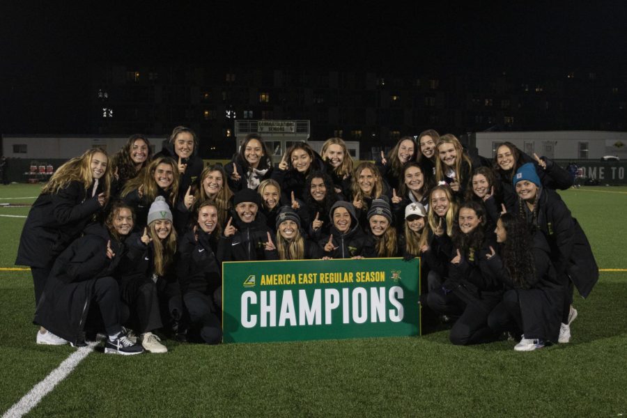 UVM women’s soccer team hold up No. 1 signs on Virtue Field as they pose with the America East Champions sign.